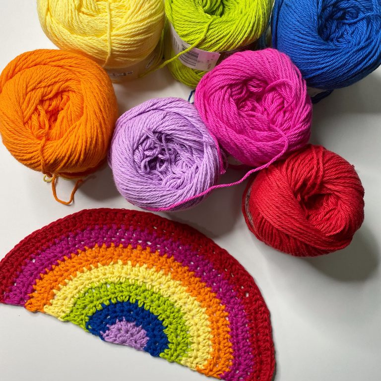 crocheted rainbow beside colorful yarn