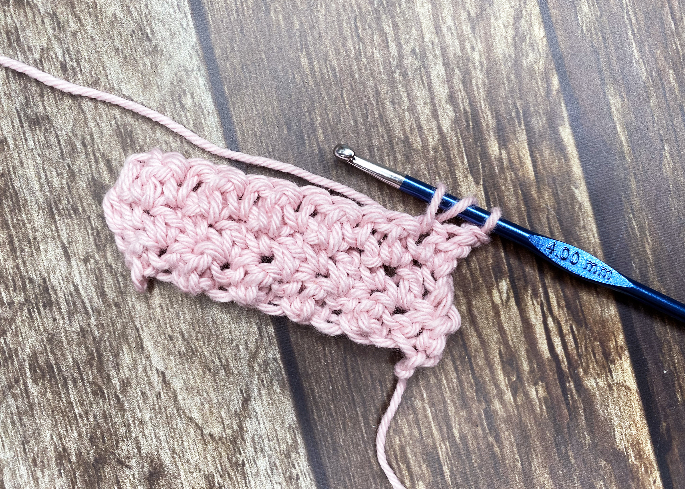 a close up of a crochet hook and a partly crocheted project using pink yarn