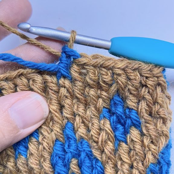 hands crocheting a blue and brown tapestry crochet chevron pattern