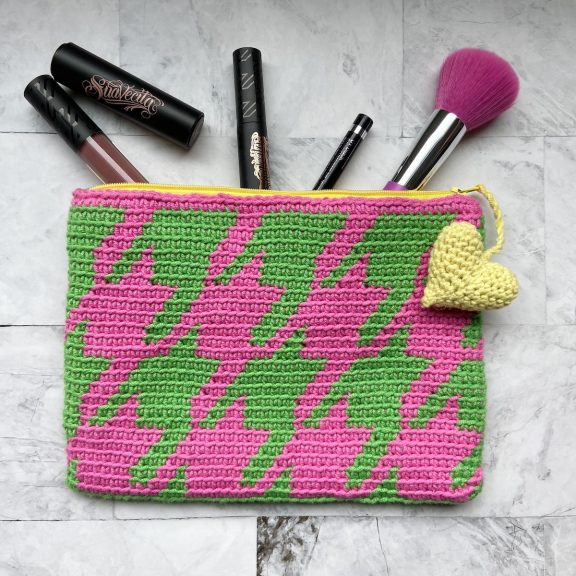 a pink and green houndstooth pouch with a heart zipper and make up spilling out of it