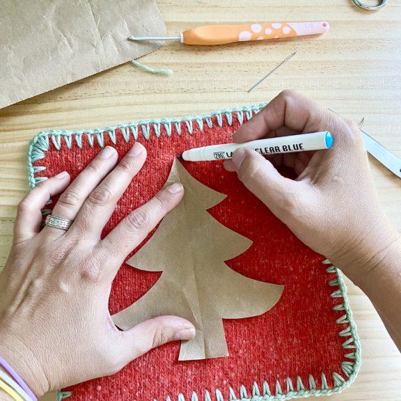 hands holding a brown paper Christmas tree template and outlining the shape with a clear blue marker