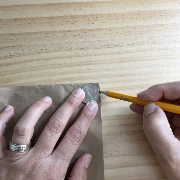 hands holding a quarter on brown paper outlining the quarter with a pencil