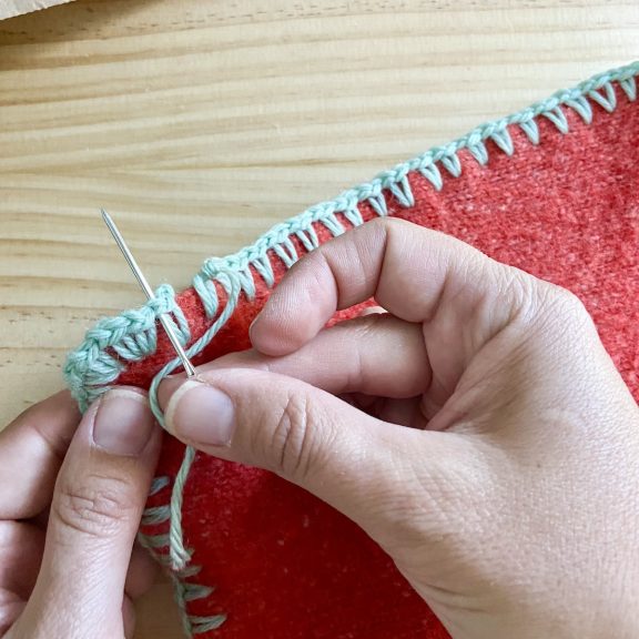 a hand holding a sewing needle to create clean embellishments on crochet edges