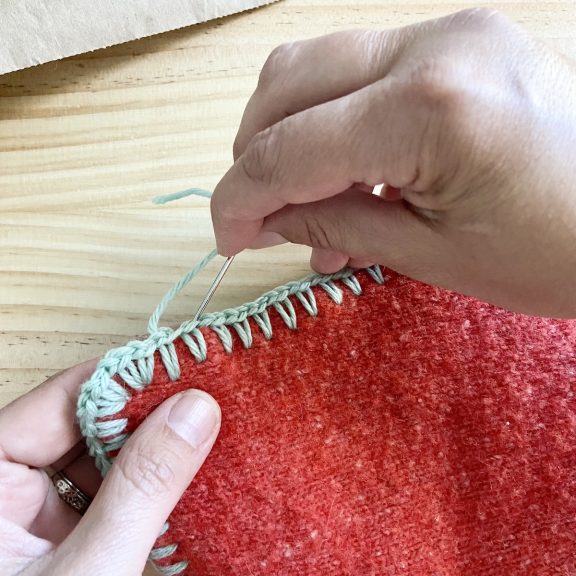 two hands holding an upcycled sweater potholder creating neat edges with a sewing needle