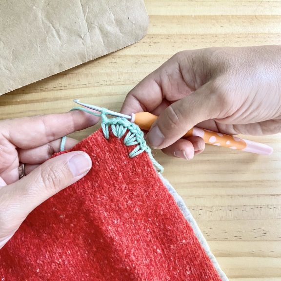 two hands holding blue yarn crocheting the corner edge of a potholder