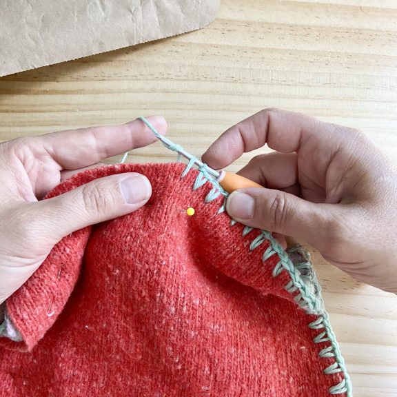 two hands crocheting SC around the edge of a potholder in blue yarn