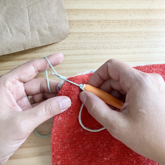 a crochet hook piercing red sweater material to begin crocheting around the edges