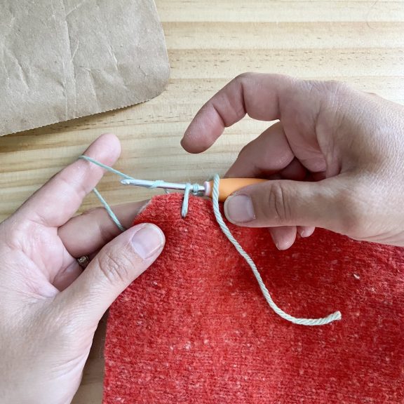 two hands holding a crochet hook and red sweater fabric stitching around the edge