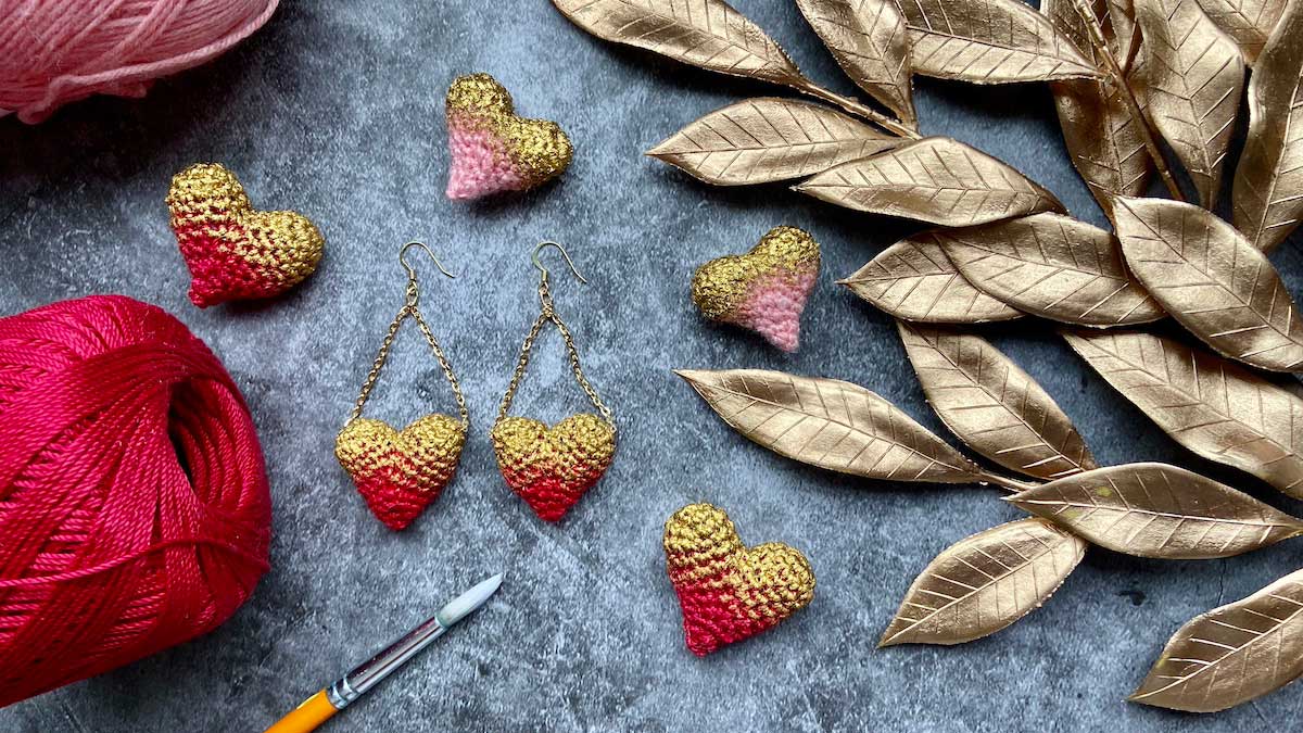 a pair of red and gold crochet heart earrings with other crochet hearts sitting around