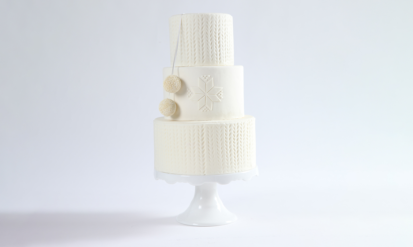 three tiered winter white cake with a snowflake and pom pom design