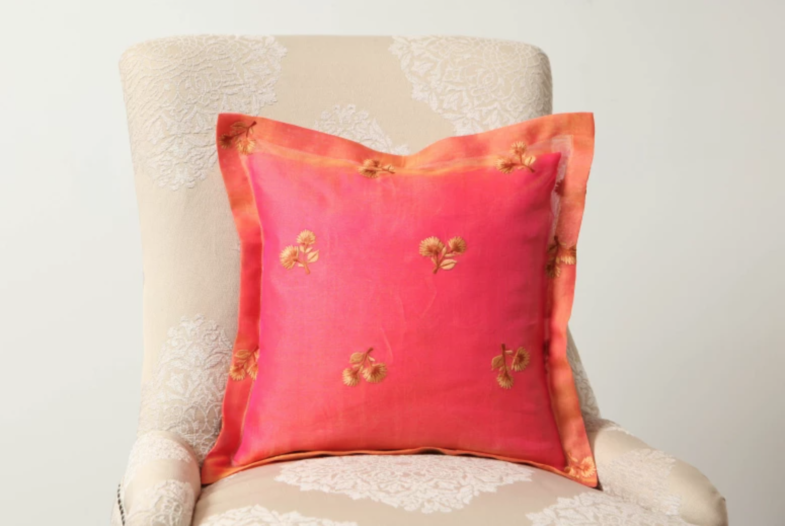 pink and orange sewn pillow on a cream chair