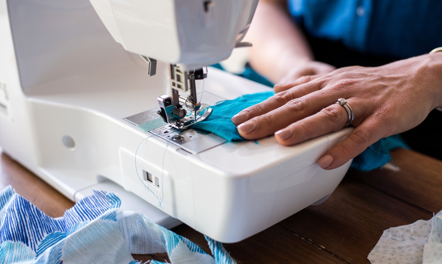 detail shot of woman sewing blue fabric