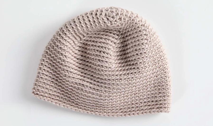 Tan crocheted beanie laid flat on a white background