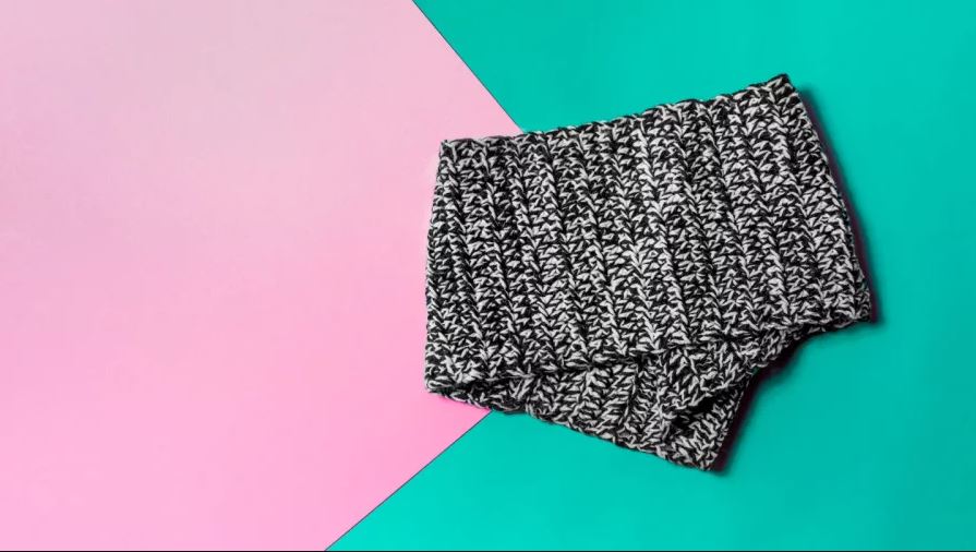 black and white crocheted cowl folded on a pink and teal background