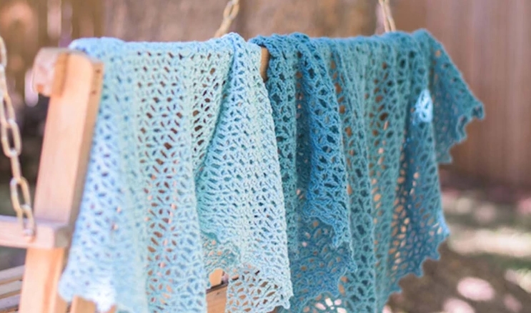 Two blue crocheted shawls draped over the back of a wooden porch swing