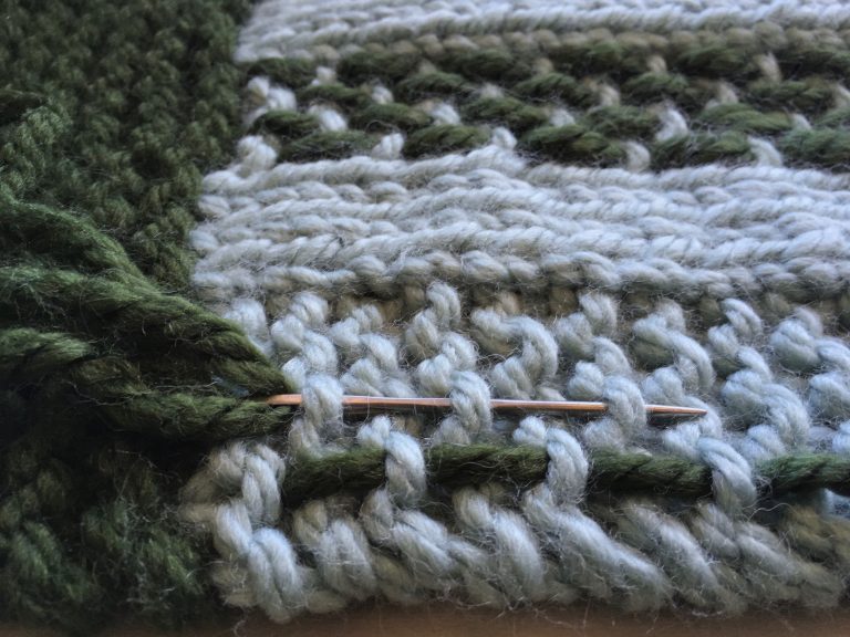 Knitting green yarn through light blue yarn on scarf
