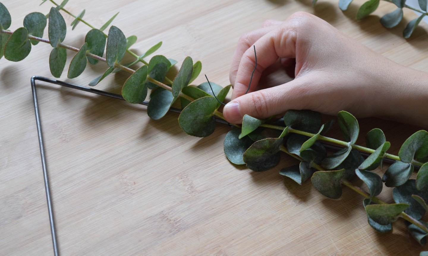 tying greenery to triangle wreath