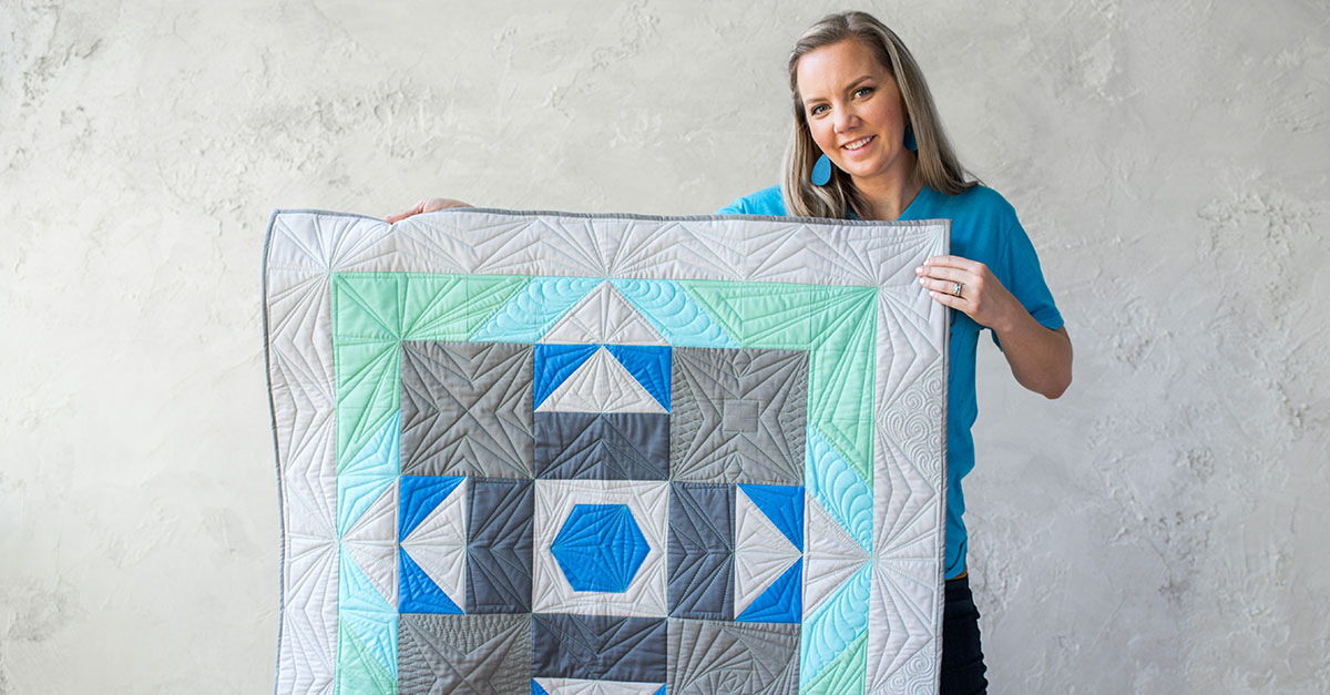 Woman holding up a blue, grey and green quilt