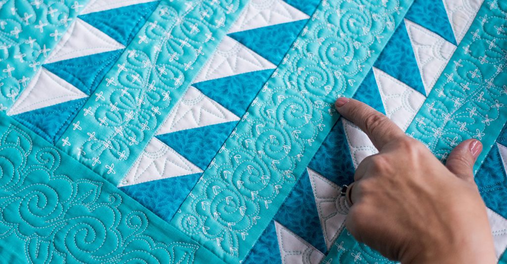 Person pointing to a stitch on a blue and white quilt
