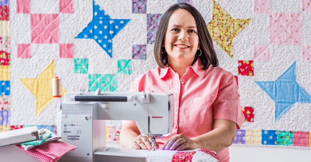 Woman using a sewing machine in front of quilt backdrop
