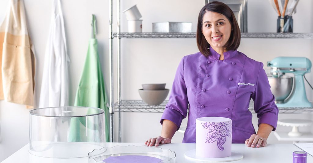 Woman in a purple chef coat with a purple cake