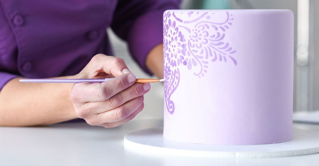 Painting a flower design on a purple cake