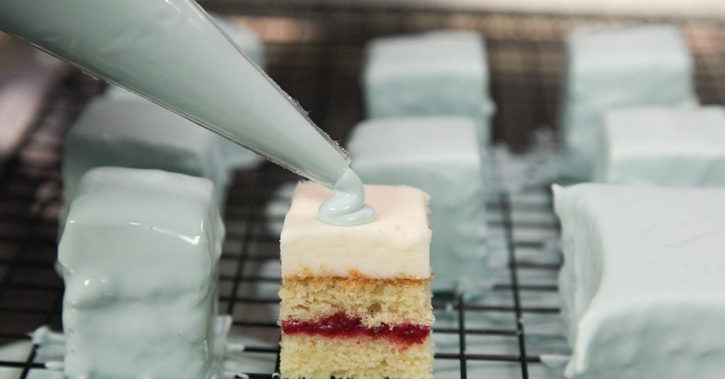 Piping light blue frosting on mini cakes