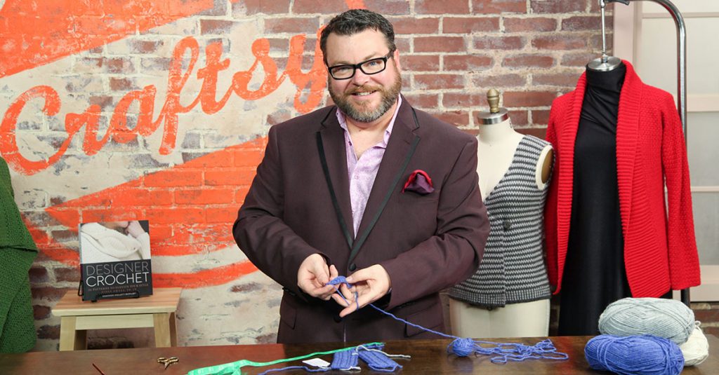 Man in glasses smiling and knitting with blue yarn
