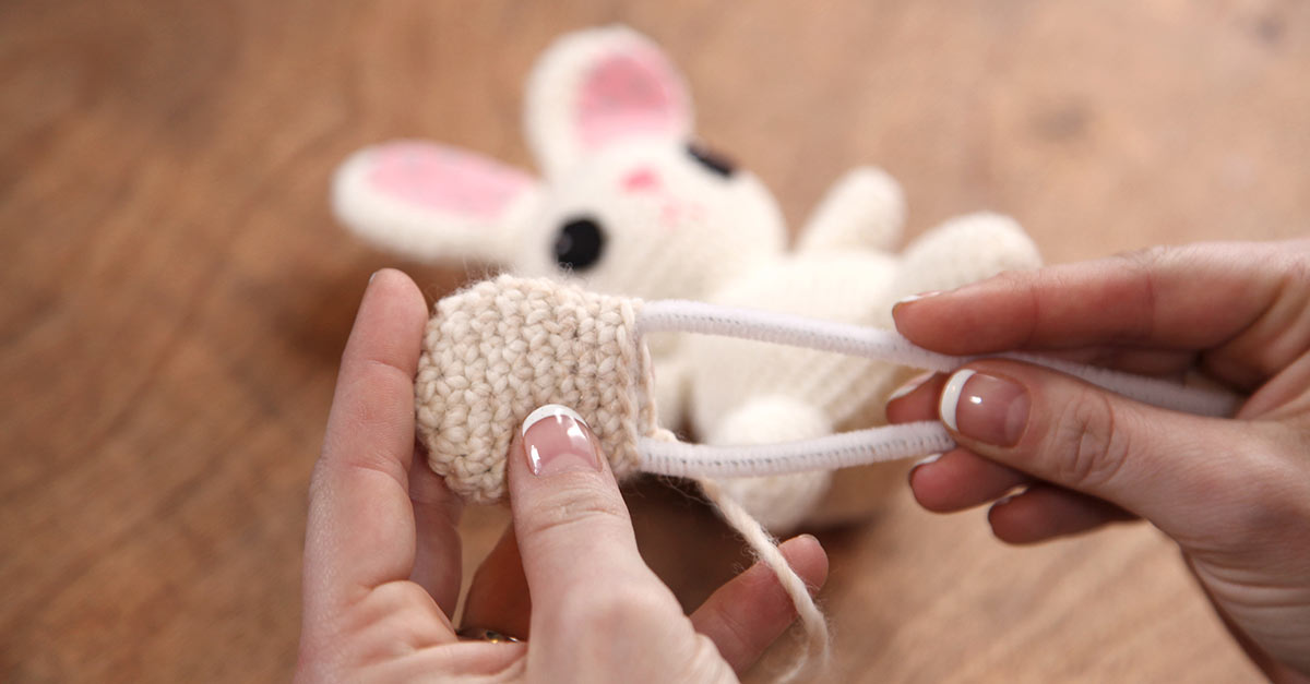 Putting a pipe cleaner in a small knit paw