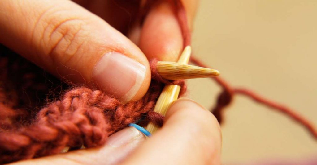 Close up of person sewing with rust colored yarn