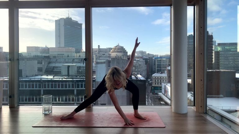 Woman doing yoga in front of large windows