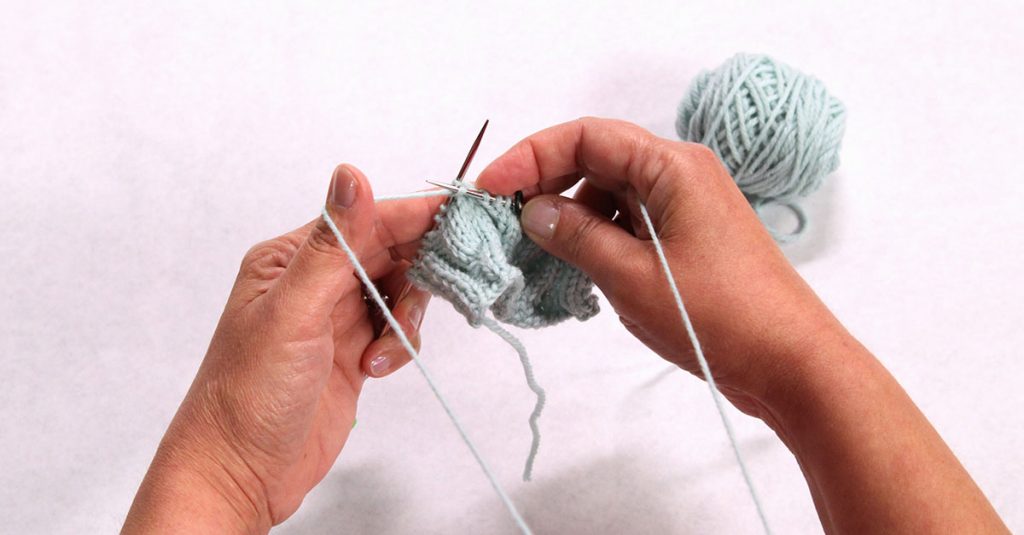 Two hands knitting with grey yarn