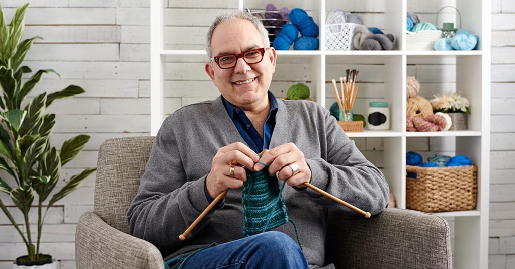 Man with glasses knitting in a chair
