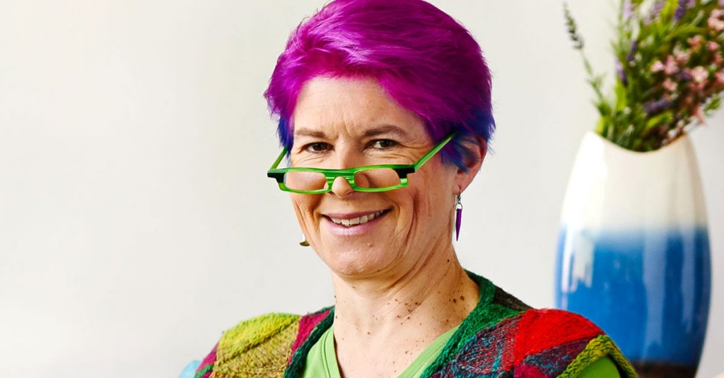 Woman with short purple hair and bright green glasses smiling at camera