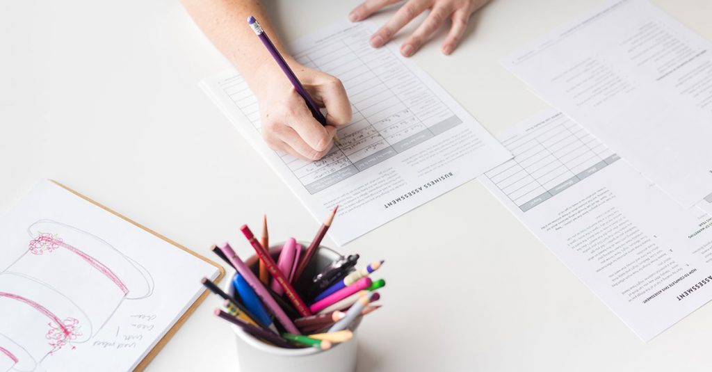 Person writing on a form with a cup of pencils around