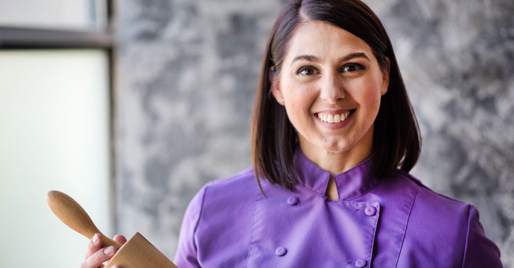 Woman in a purple baker's jacket holding a rolling pin