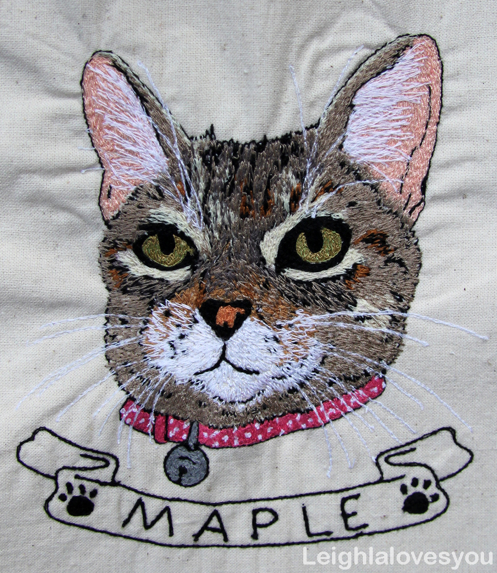 Embroidered portrait of tabby cat with maple written below