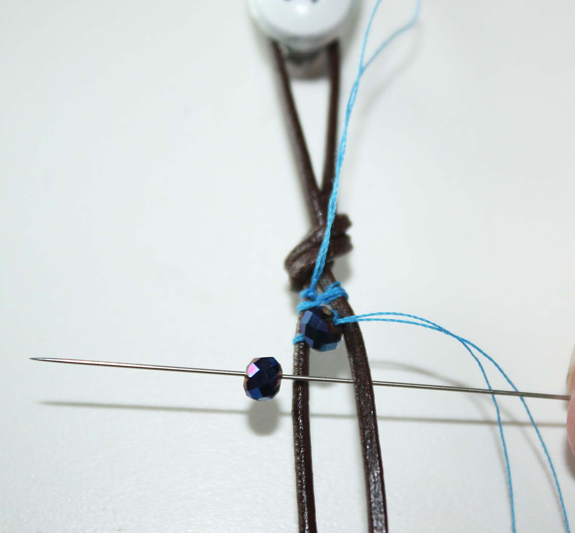 Add second bead by threading under leather cord up through center of cords, add bead and thread out over top of the other leather cord.