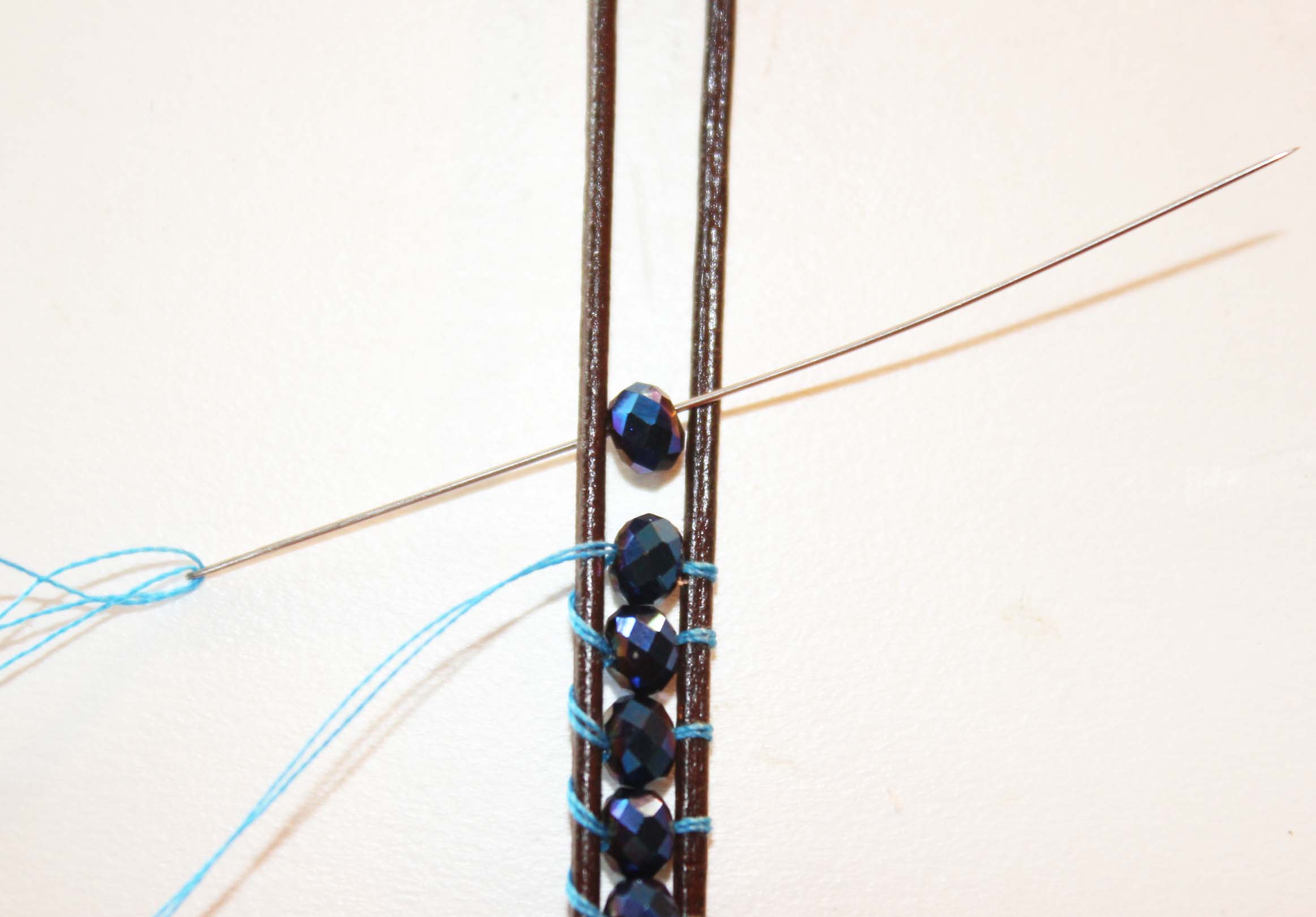 Add the next bead by feeding thread under the leather cord and up through center of the two cords. Add the bead.