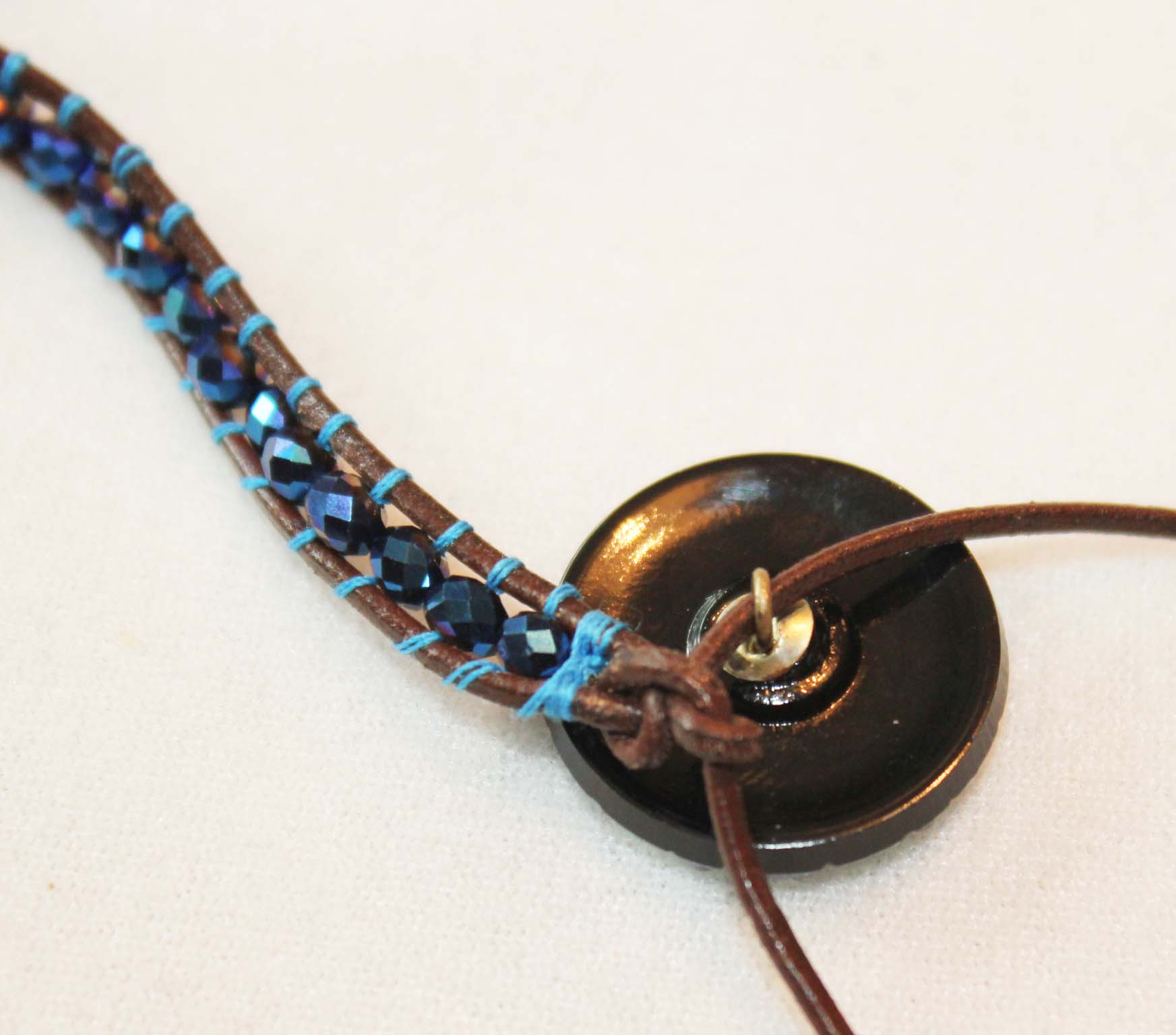 Tie leather into a knot and add the button to one leather cord
