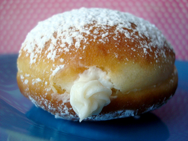 Finishing a cream filled doughnut with confectioner's sugar 