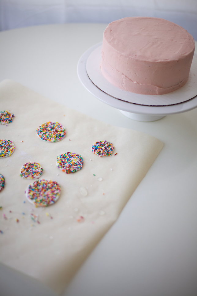 Adding colorful rainbow sprinkles to a simple buttercream layer cake