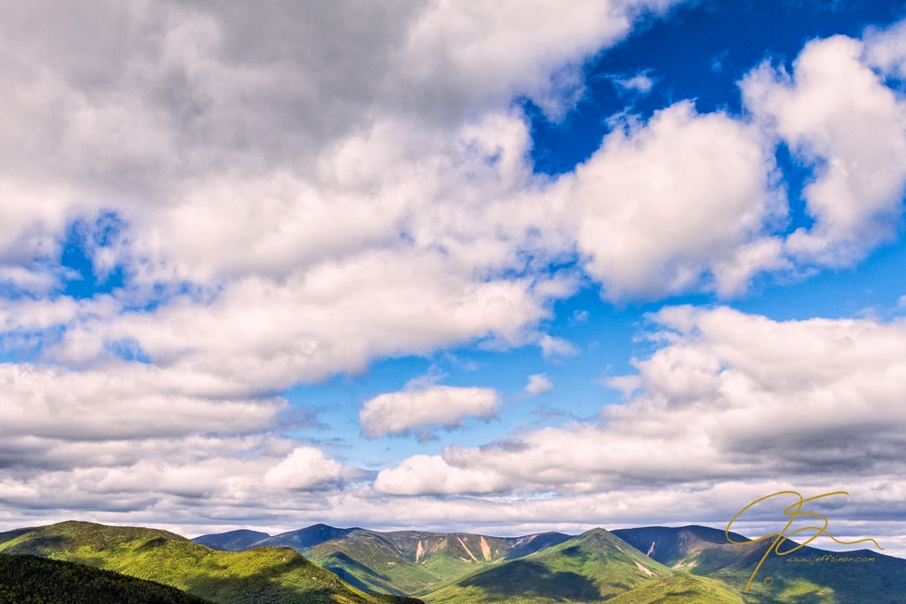 A sky full of billowy white clouds drifts over the New Hampshire mountains.
