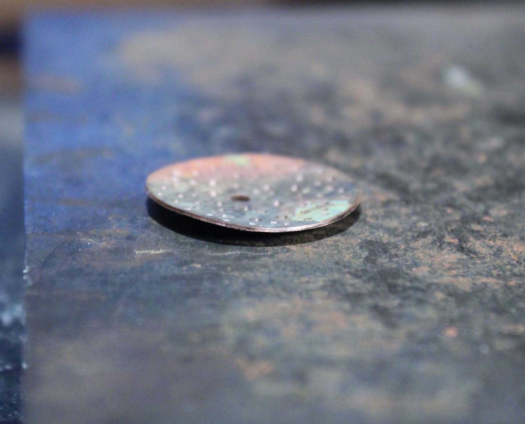 A copper disc has been textured, causing it to curve upward.