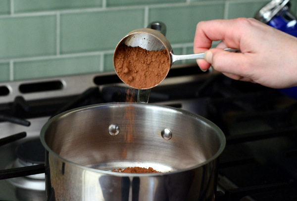 Pouring cocoa powder into a pot on the stove