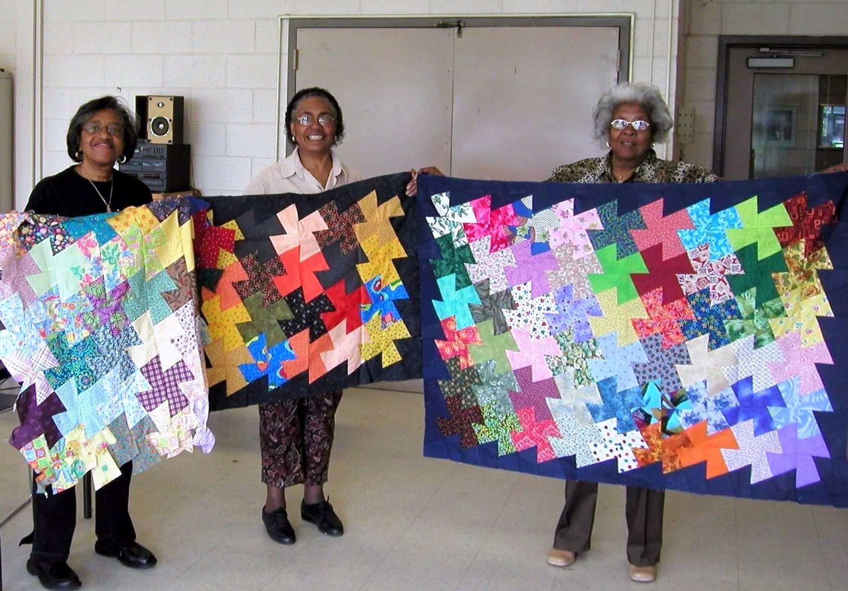 Quilters holding up finished quilts