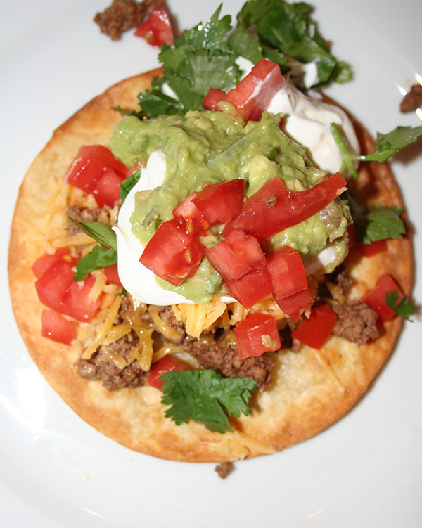 Tostada topped with tomatoes, sour cream, cilantro and tomatoes