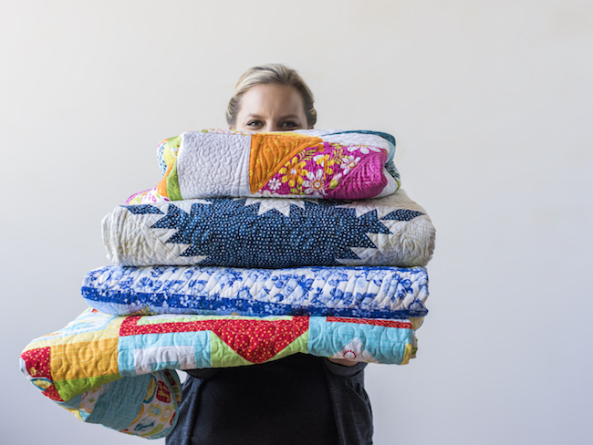 Angela Walters Holding a Stack of Quilts