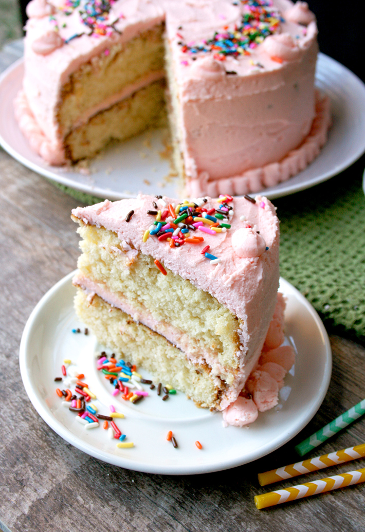 Slice of white birthday cake (with pink frosting) cut out of full cake with sprinkles on top