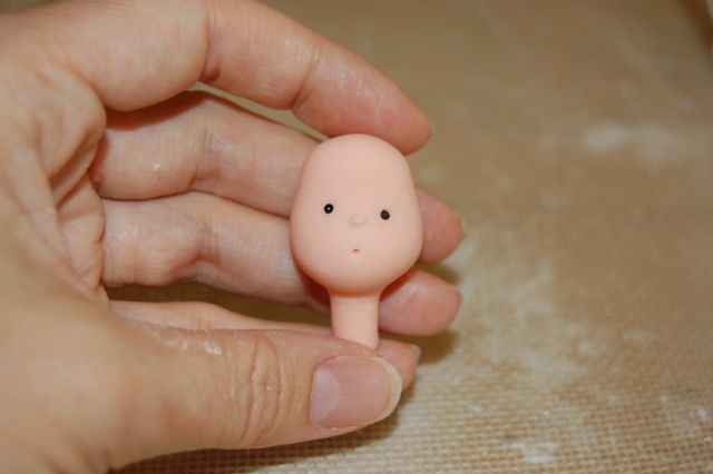 Hand Holding Fondant Baby Head with Little Nose and Sprinkle Eyes